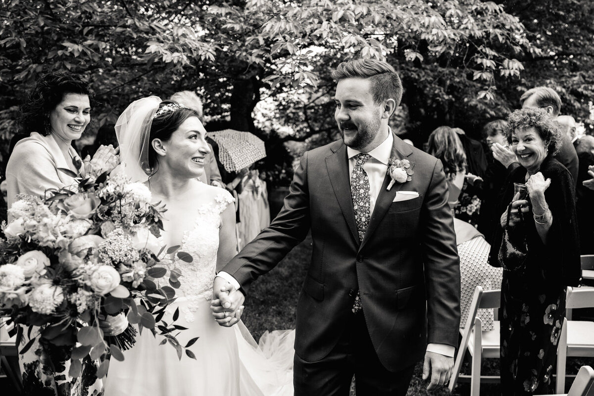 A newlywed couple holding hands and walking back up the aisle 