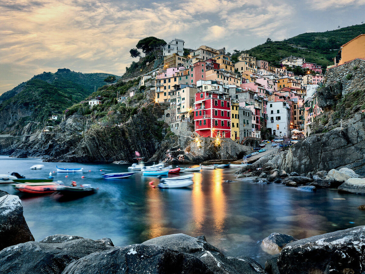 Langzeitbelichtung des Hafens von Riomaggiore mit beleuchteten Booten und bunt beleuchteter Häuserkulisse – stimmungsvolle Küstenfotografie mit urbanem Charakter