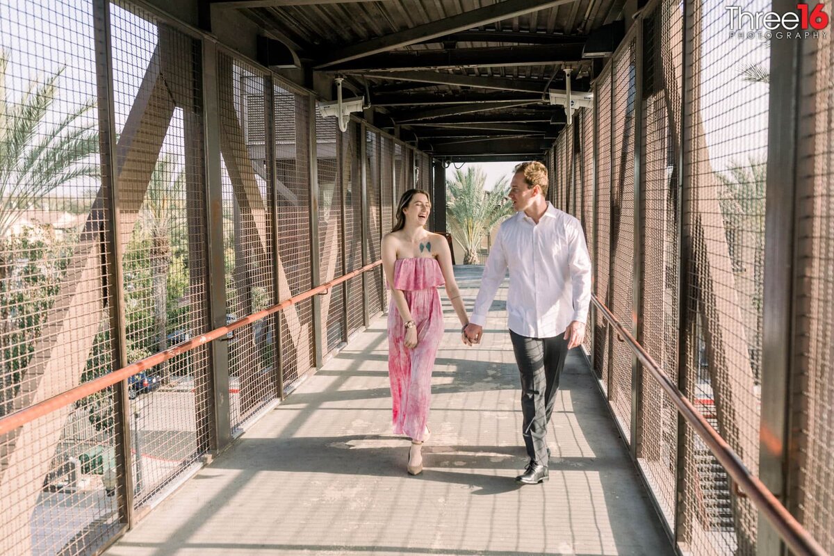 Engaged couple walk across the bridge holding hands