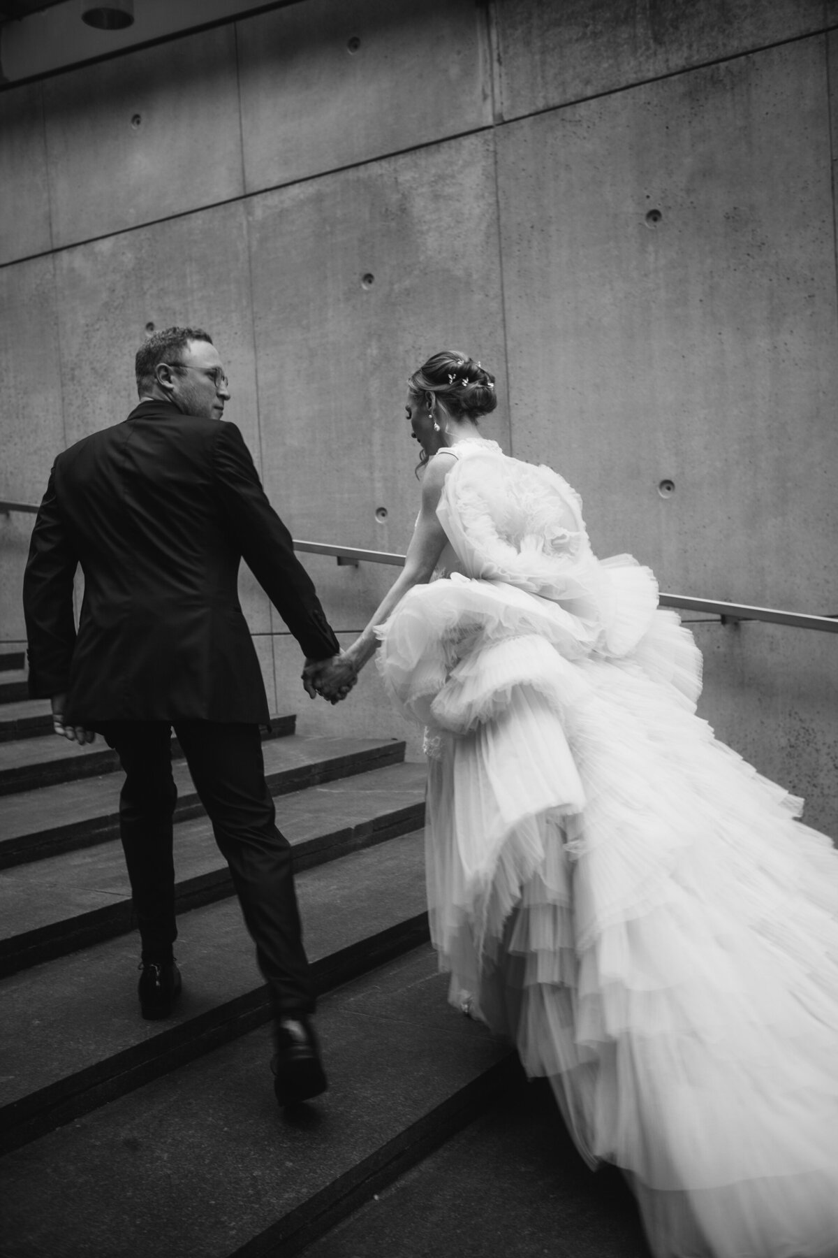 Bride and groom walking up stairway together, black tux couture wedding gown