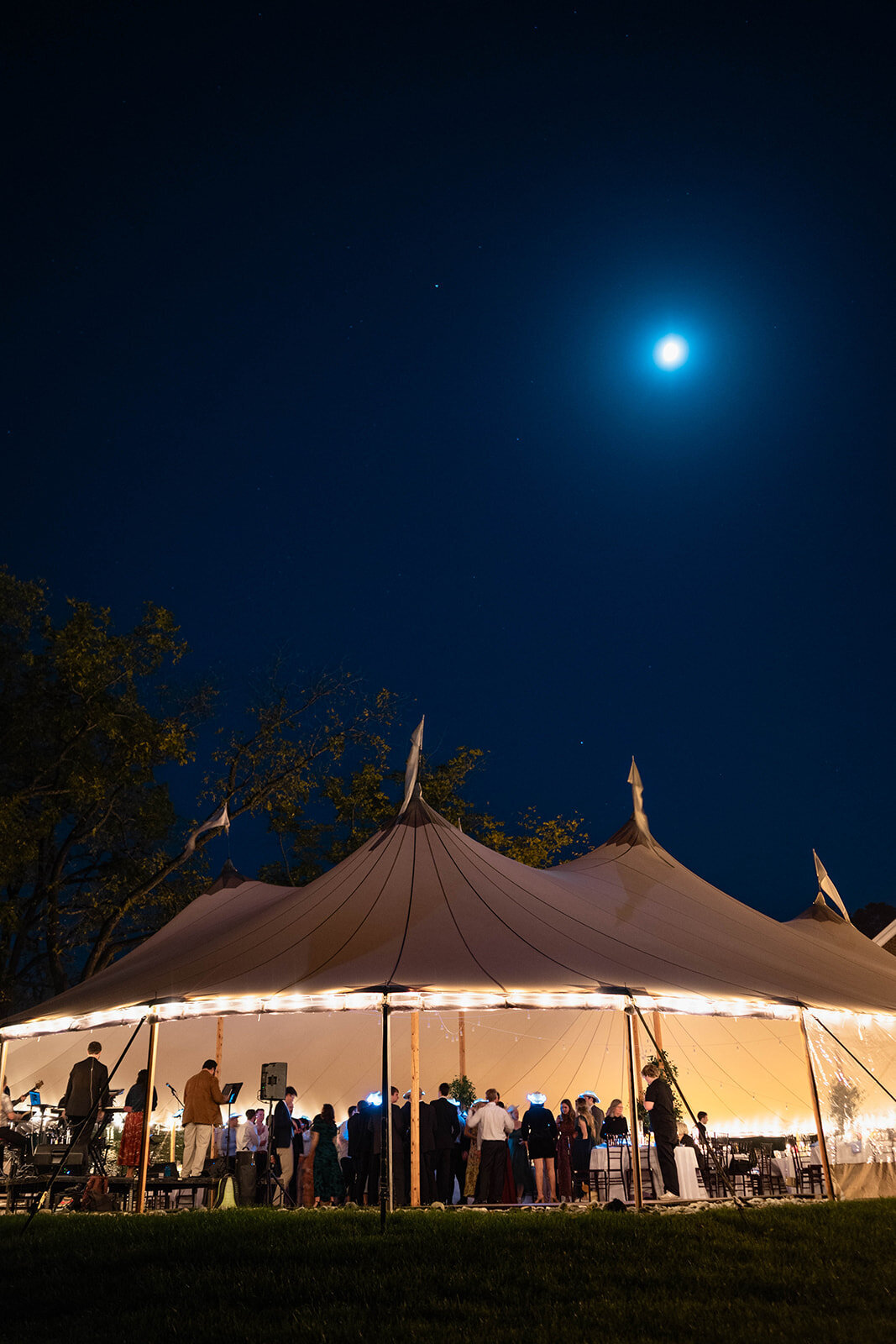 Wedding guests sit under sailcloth tent nighttime