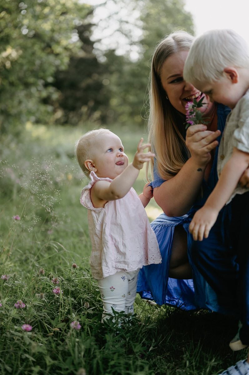 Mamma och två syskon kollar på blomma tillsammans och de ler.