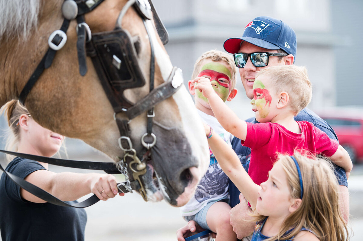 a little boy with face paint getting excited while he pats a horse during a corporate children's event.  Captured by Ottawa Event Photographer JEMMAN Photography COMMERCIAL