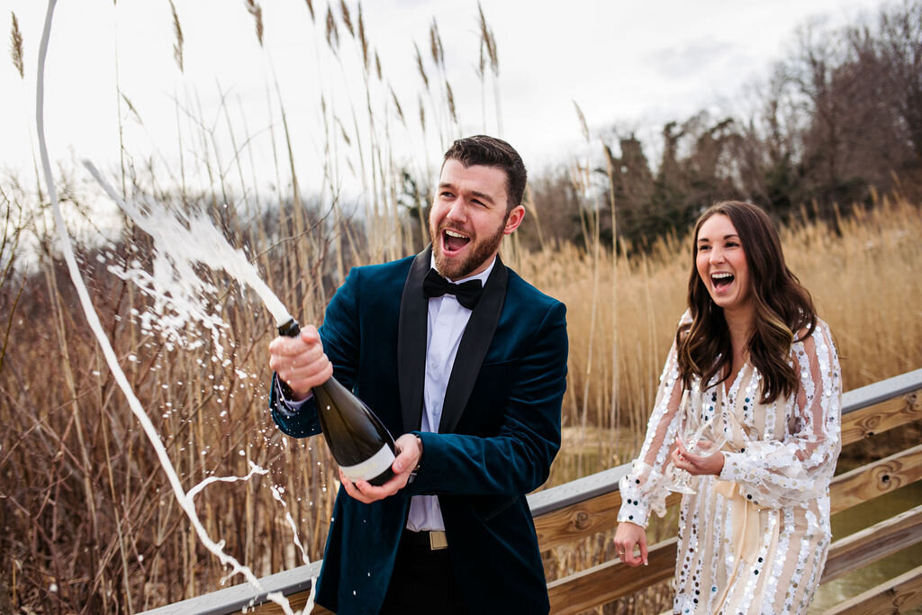 A couple spraying a bottle of champagne and laughing