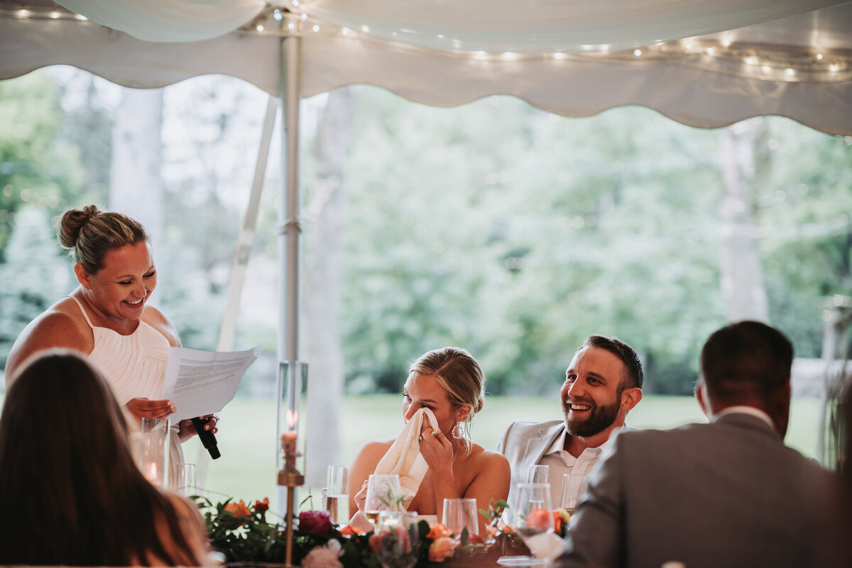 Bride wiping tears as her sister and maid of honor gives a speech.