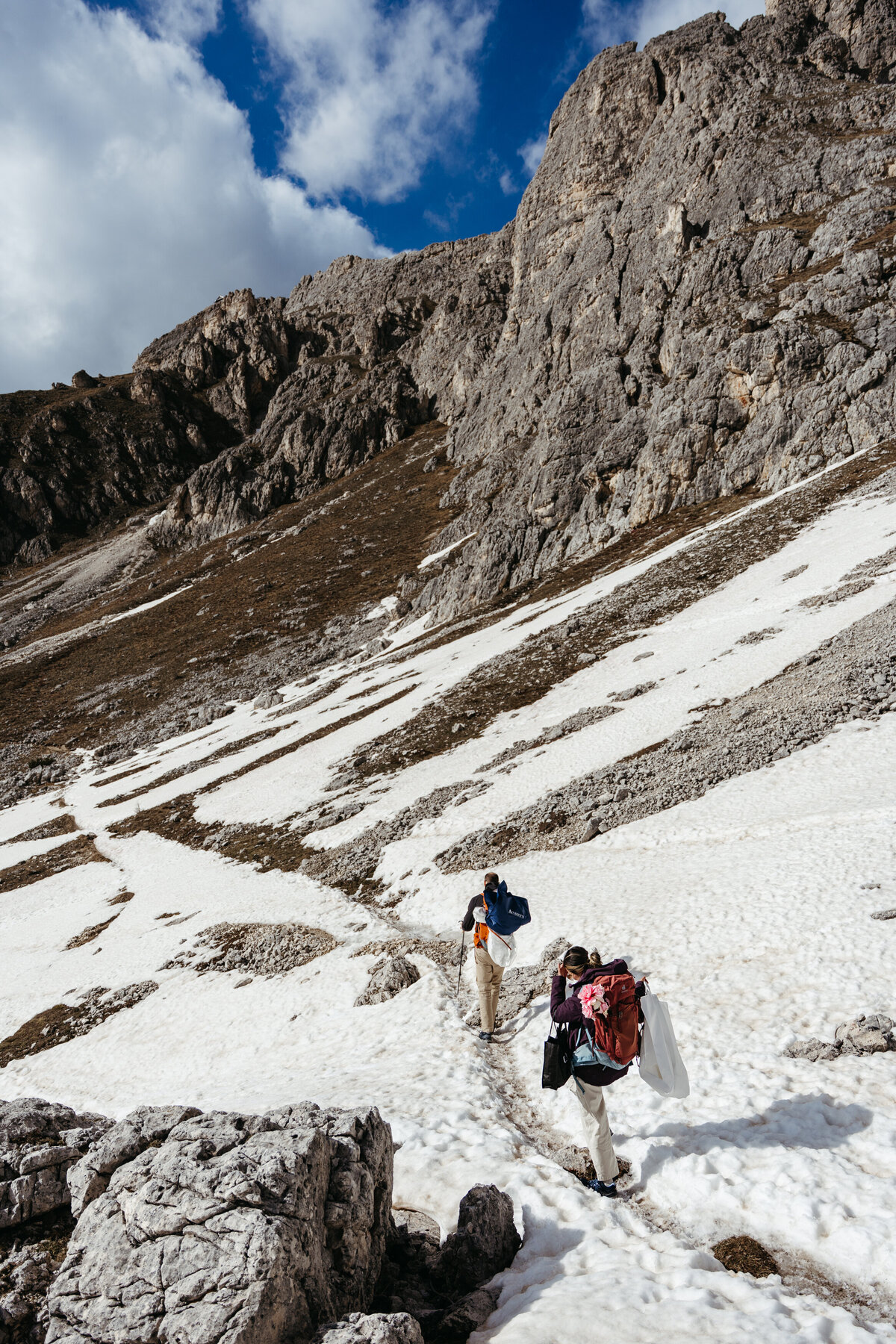 Bride and groom walking mountain trail with snowy peaks behind