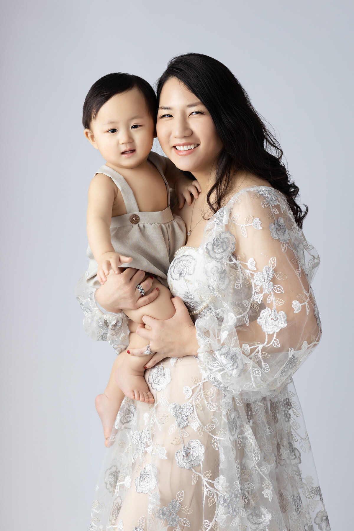 Dallas baby milestone photographer captures a loving moment between a mother and her son, both smiling with joy, against a light background.