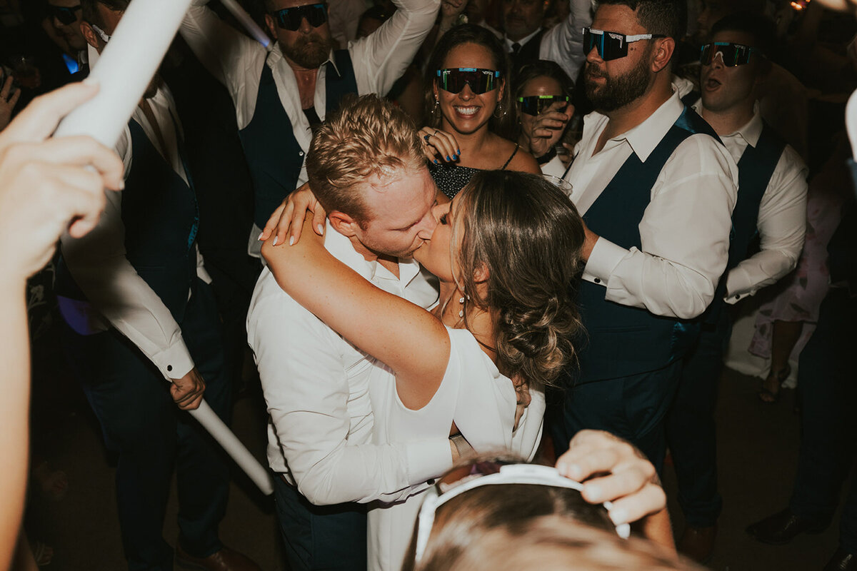 Alana and Ryan kissing each other on their wedding reception party while guests cheering them