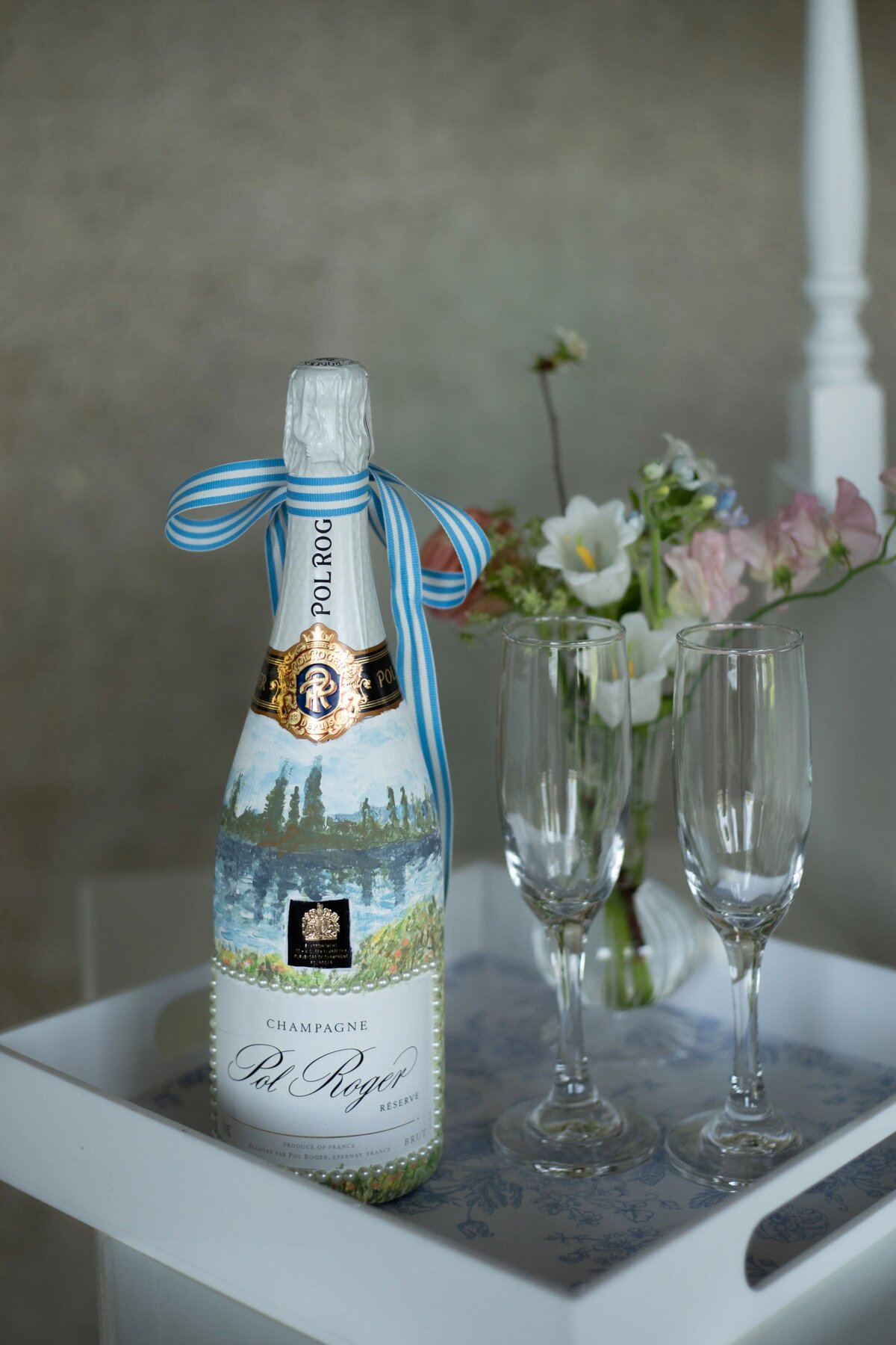 Elopement Wedding Packages Rhode Island | Kelsey Sheehan Photography Timeless Rhode Island Weddings | A bottle of Pol Roger champagne with a blue ribbon stands next to two empty flutes on a tray. Soft pink and white flowers are in the background.