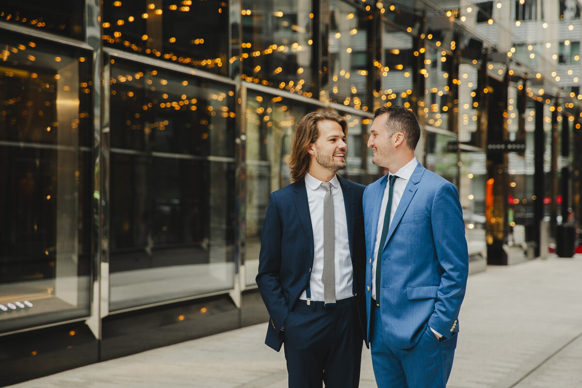 Newlyweds standing on a sidewalk with their arms around each other smiling 