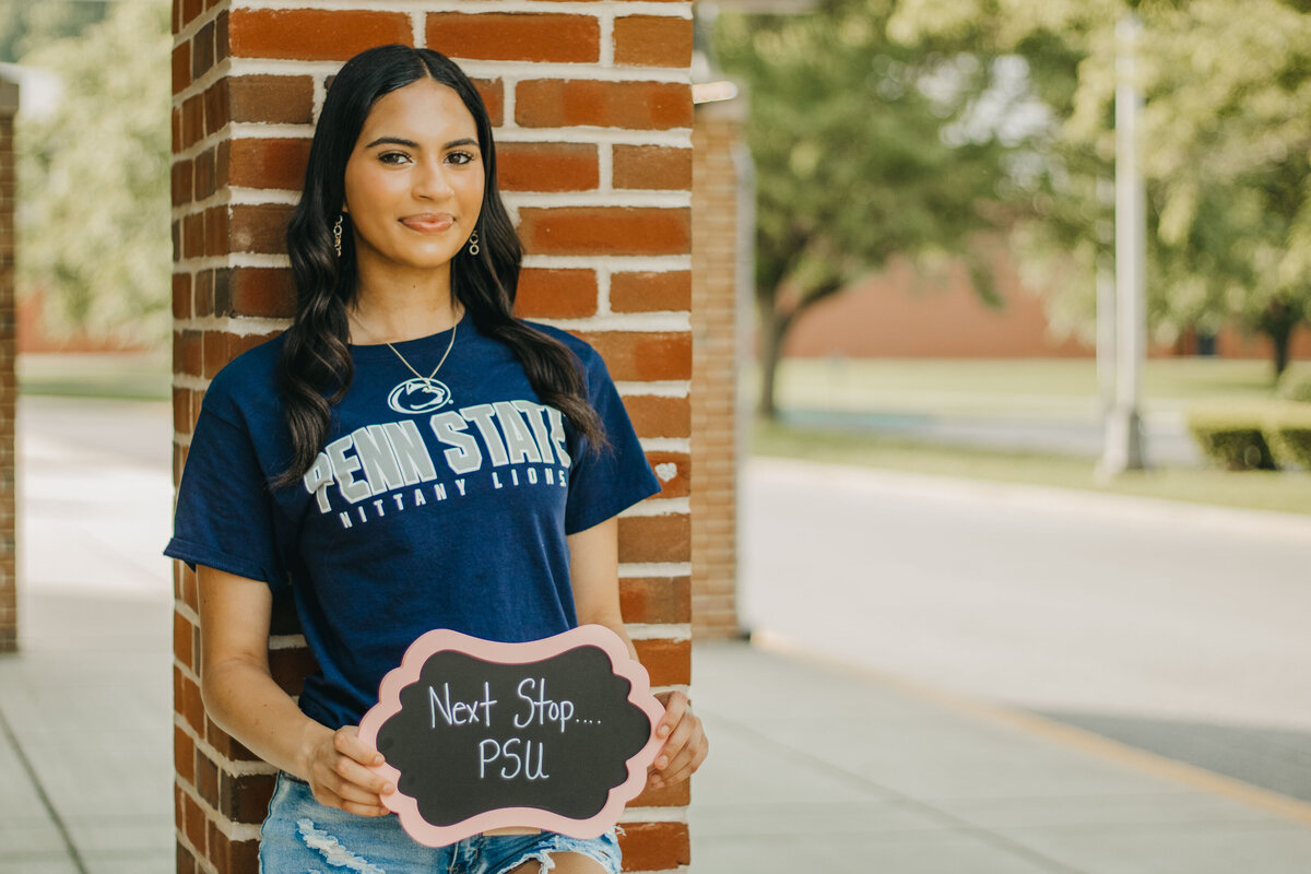 semior girl leands against building holding a sign that says "Next step, PSU"