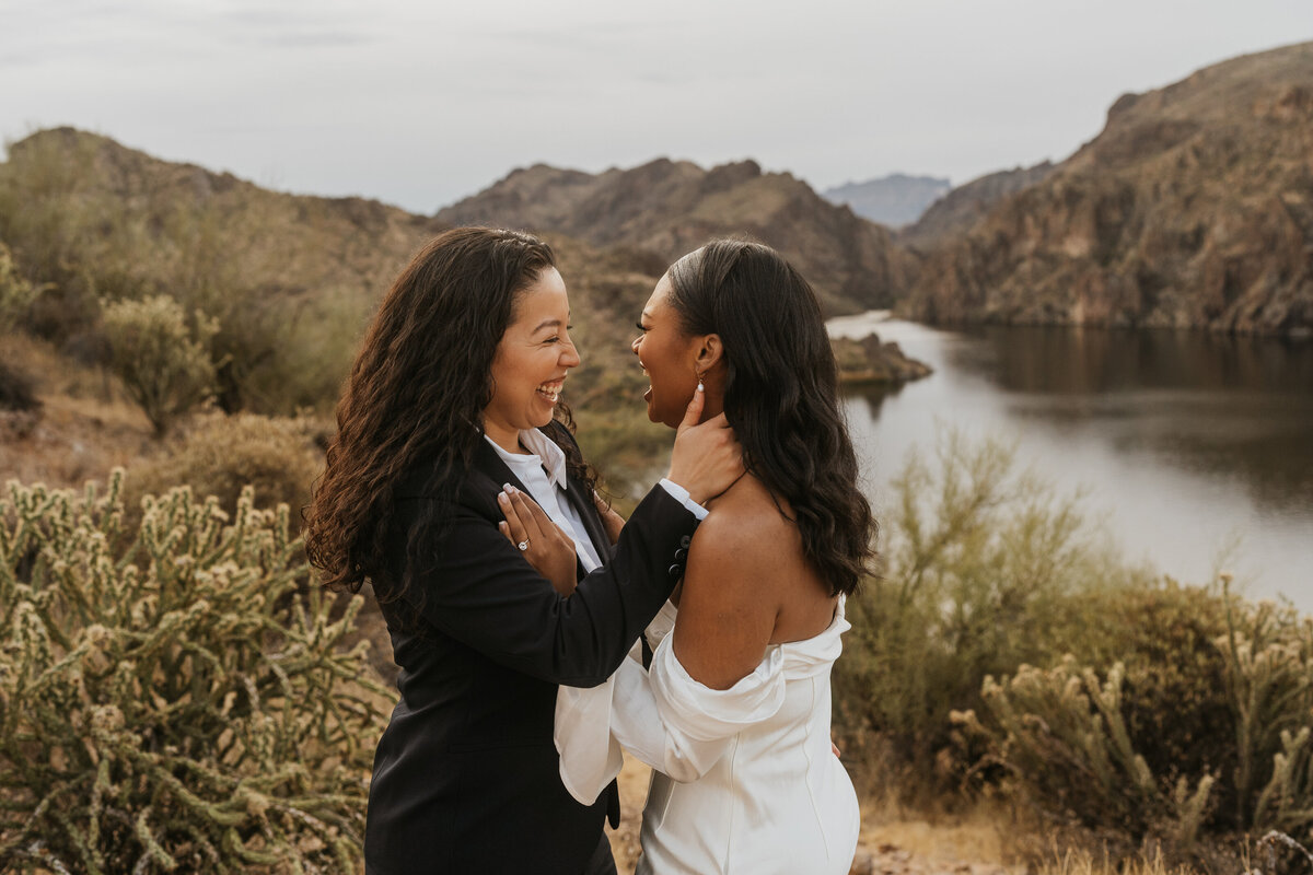 A newlywed couple laughing as they reach towards each other 