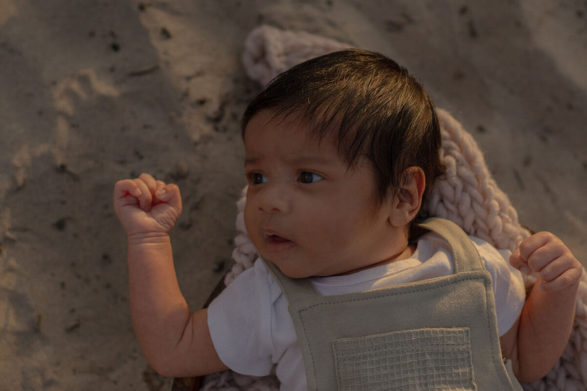 Close-up of a newborn baby lying on the sand, captured during a family beach session