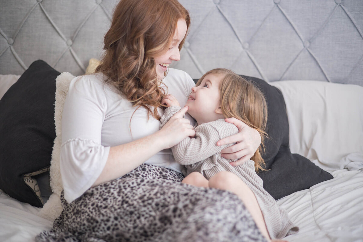 redheaded mom playfiully touching her young toddler daughter's chin.