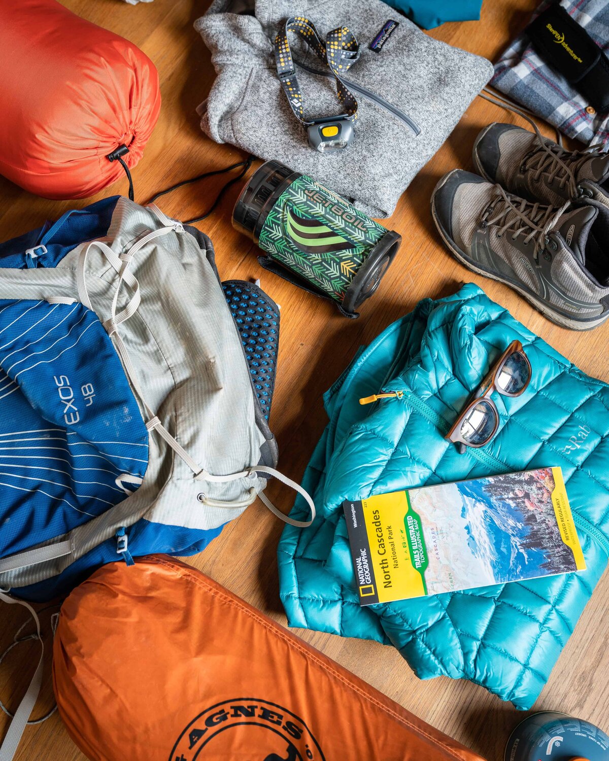 Hiking boots, coats, tents, backpacks, and gear spread out on an orange mat