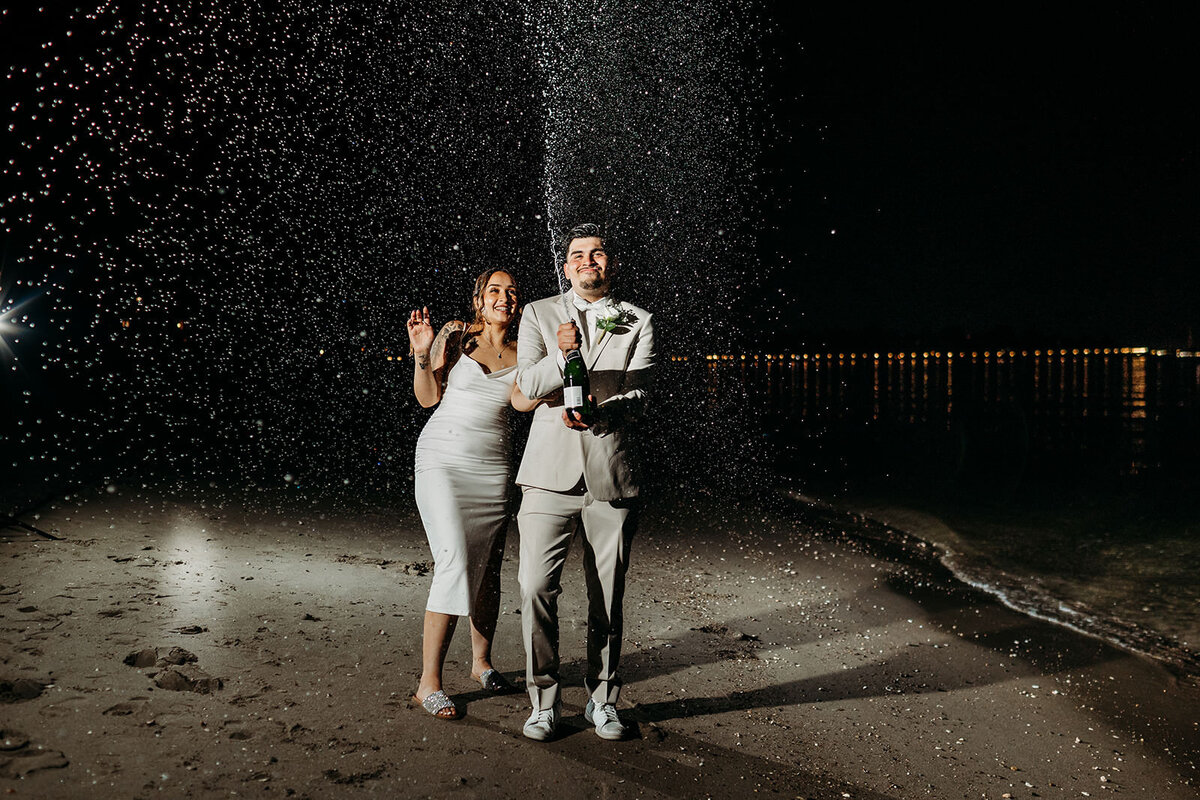 Engaged couple shoots bottle of champagne on the beach