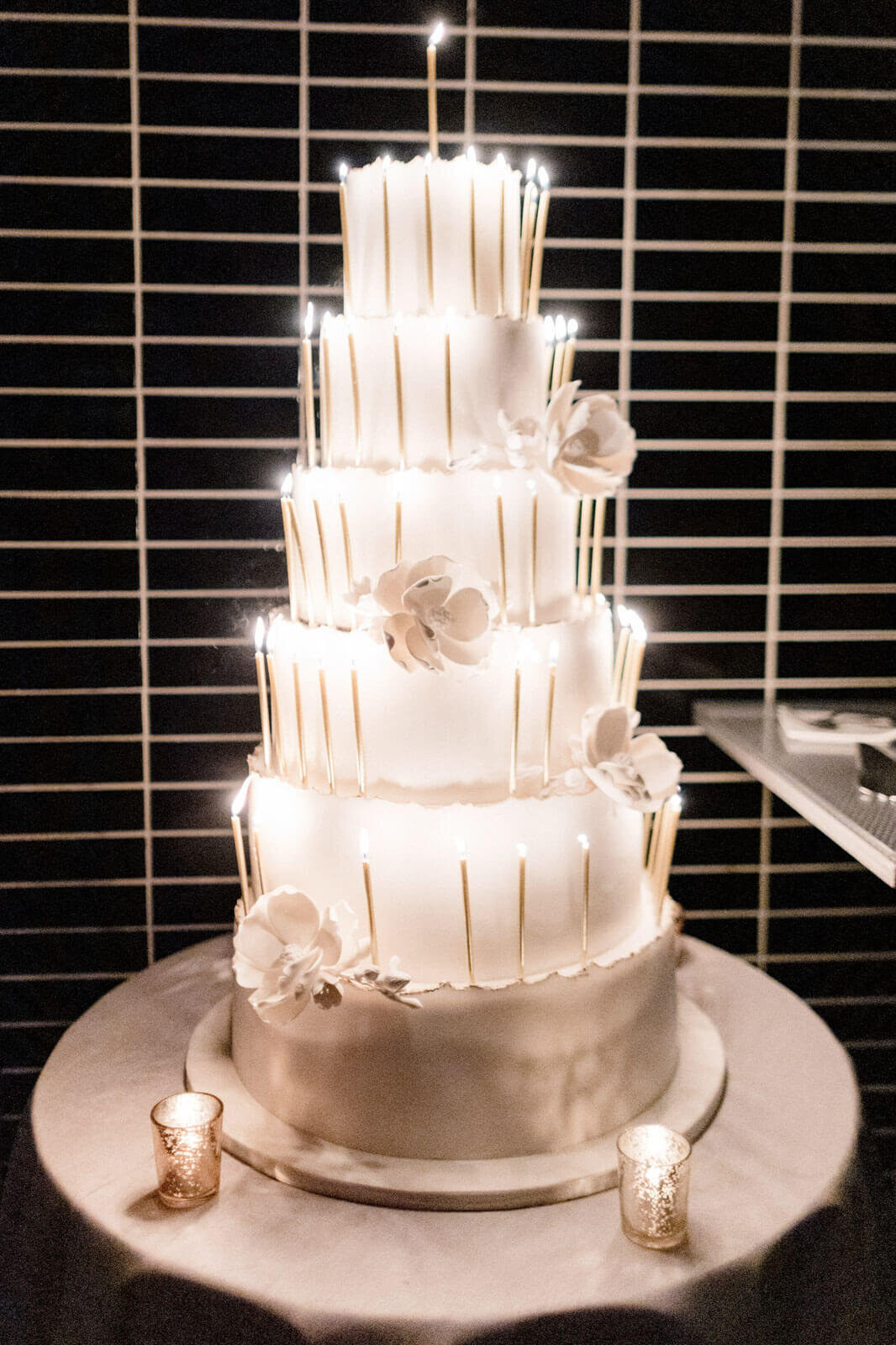 A huge, 6-layer white, monochromatic wedding cake with white candles in The Skylark, New York. Wedding Image by Jenny Fu Studio