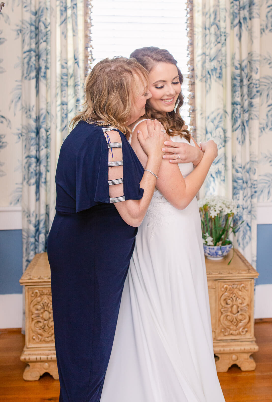 Mother hugging bride in bridal suite while getting ready for her wedding.