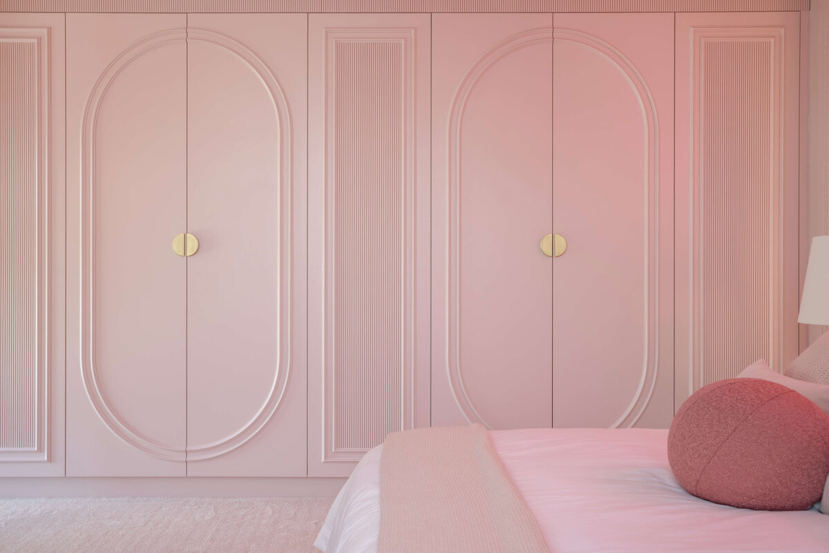 Built-in closets in a girl's pink bedroom. The closets are pink with intricate molding and gold handles.