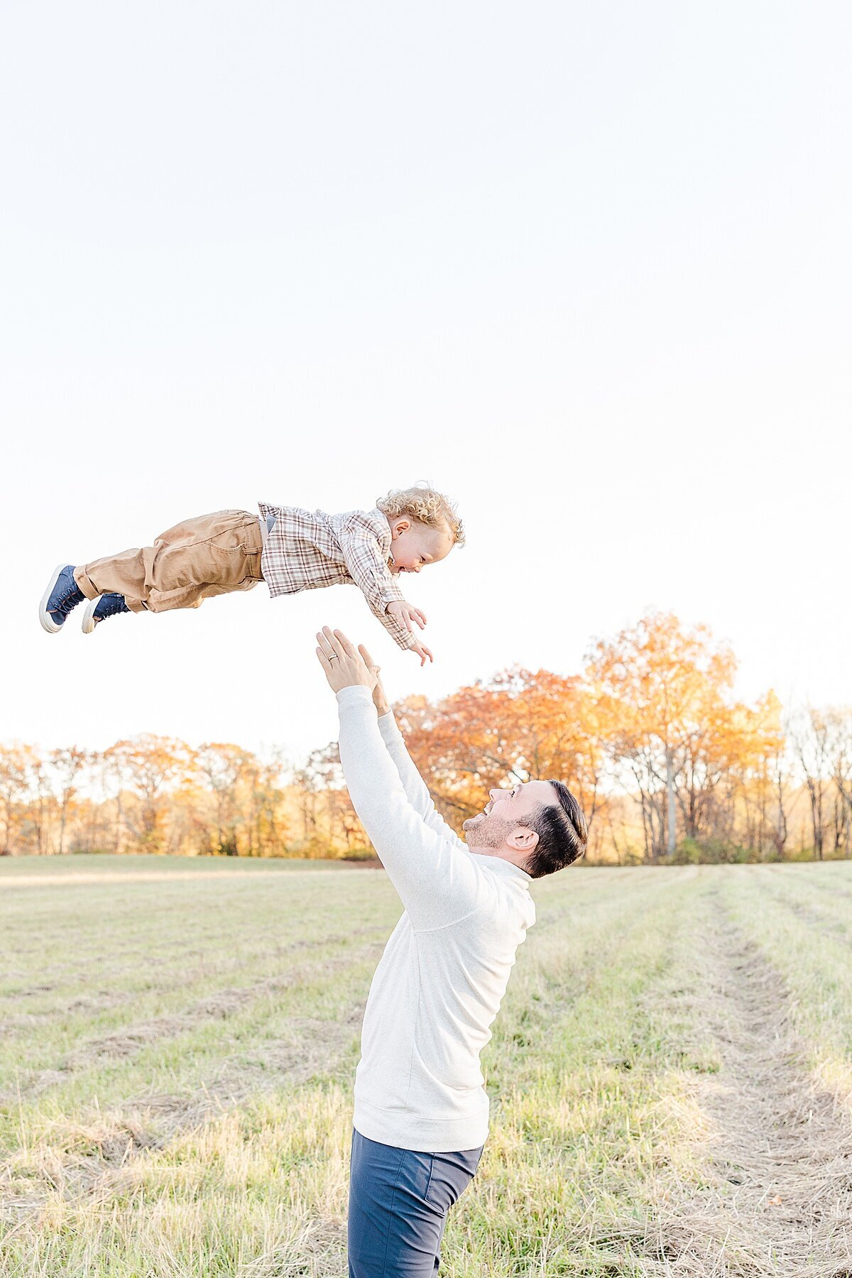 father throws toddler in the air  during winter maternity photo session with Sara Sniderman Photography at Heard Farm in Wayland Massachusetts