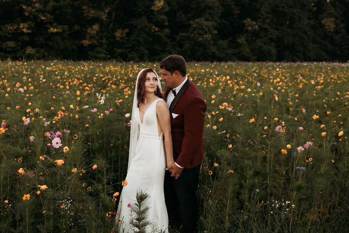 Bride in white dress with groom in red suit in a field of flowers