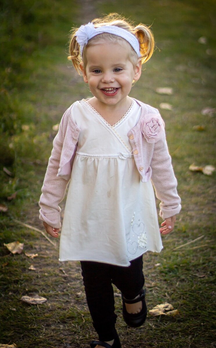 a little girl in a white dress with a pink cardigan playing in a field