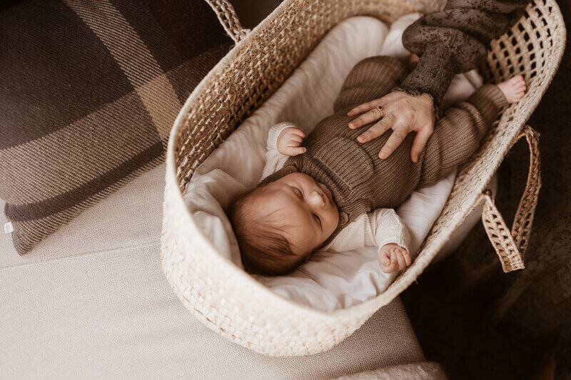 newborn baby boy laying in Moses basket while mom holds his stomach