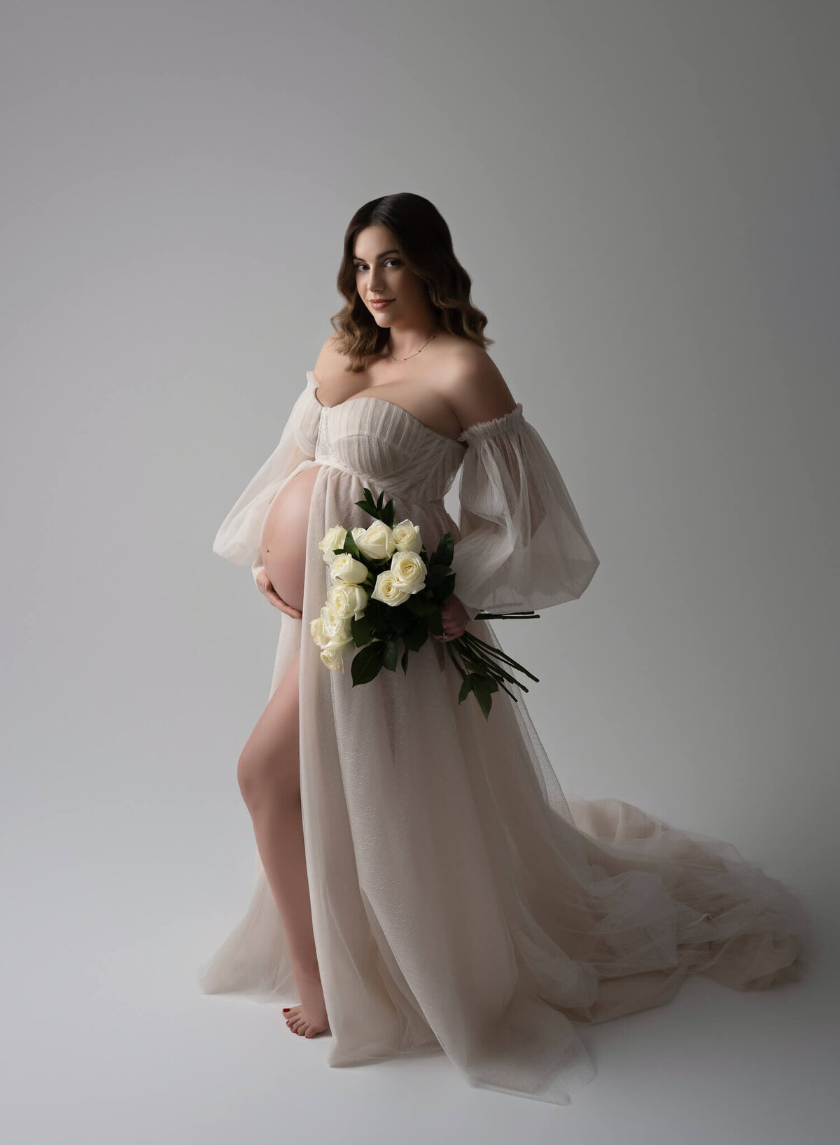 smooth ivory tulle maternity gown worn by pregnant woman holding bouquet of roses
