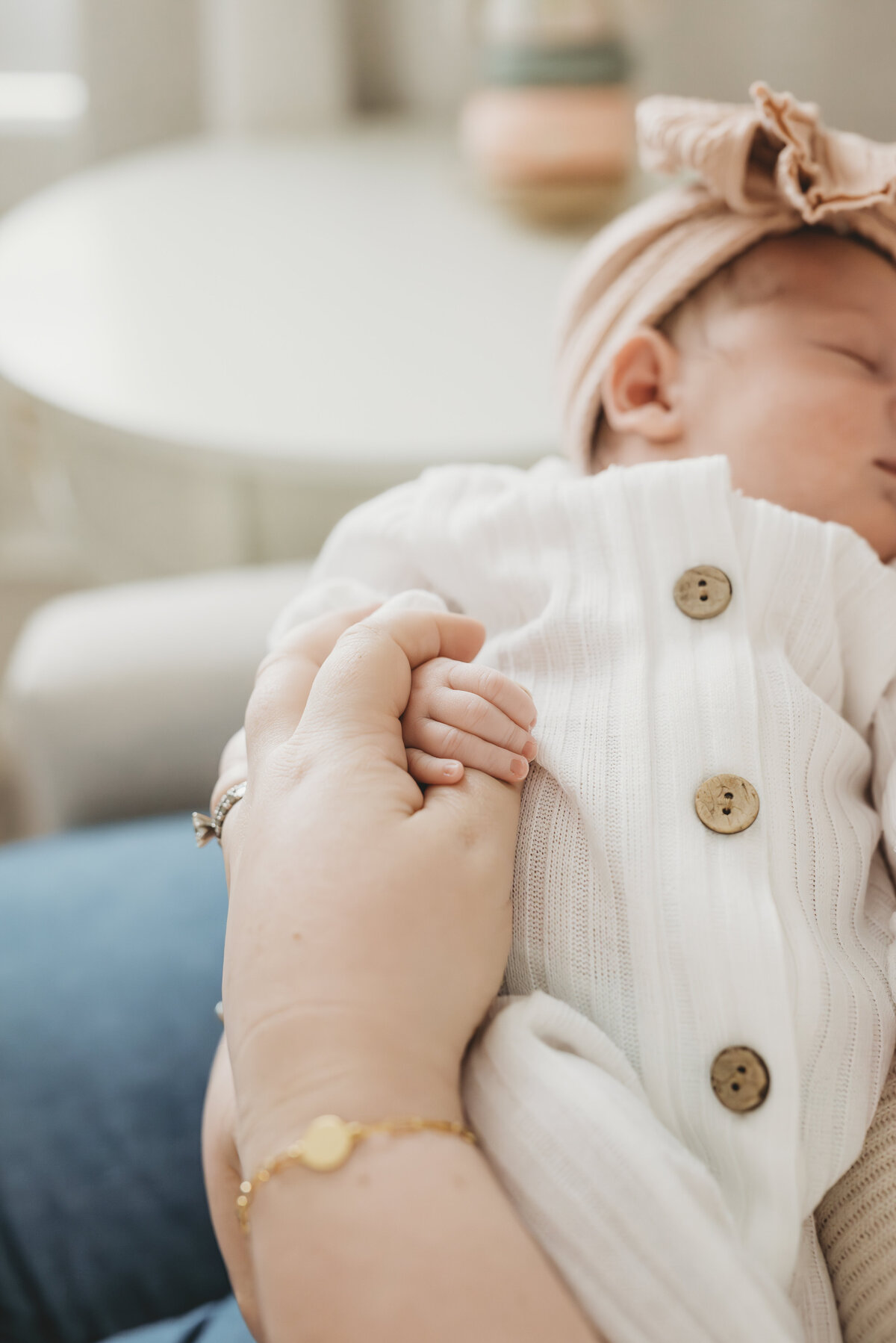 Newborn baby resting in a parent’s arms, dressed in a white romper during a cozy Kansas City newborn session.