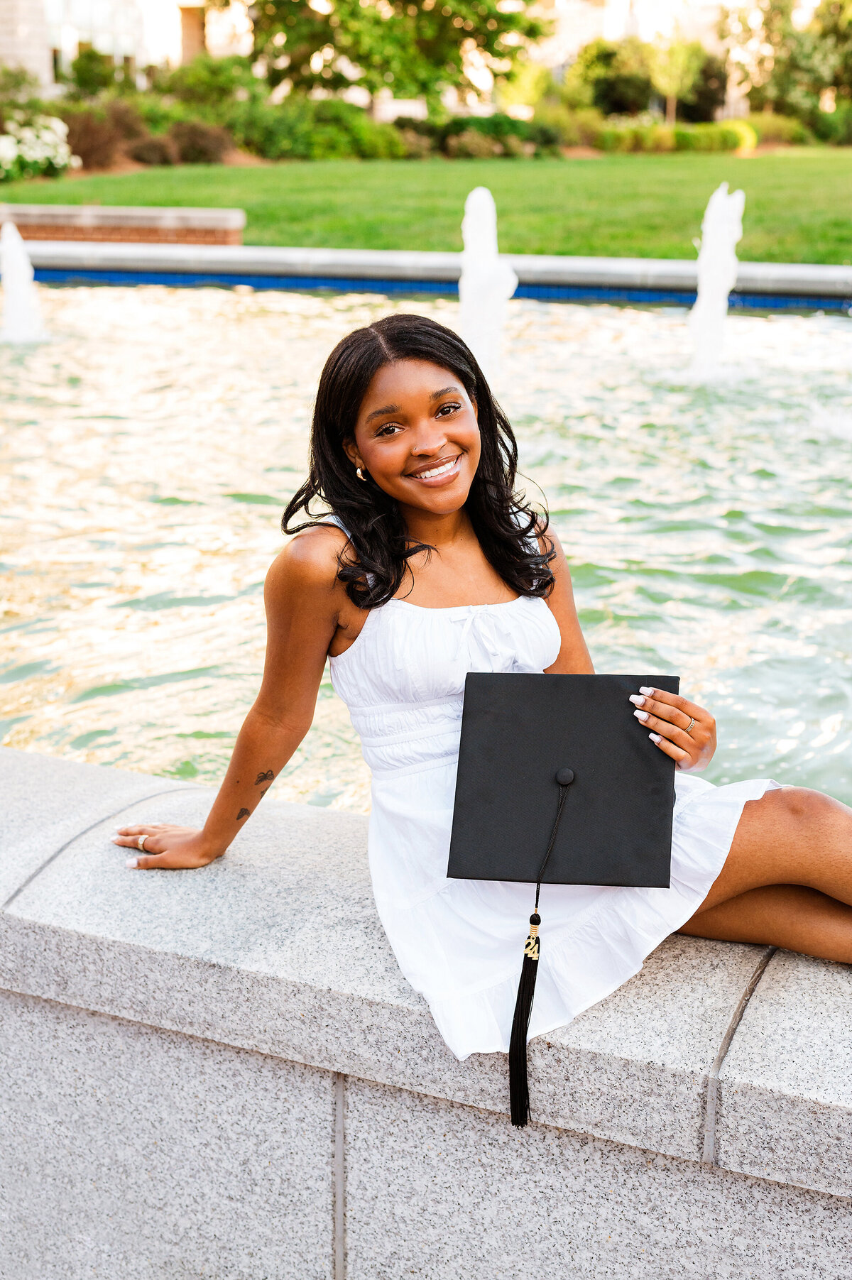 Senior girl at Belmont sitting near fountain and holding her graduation cap