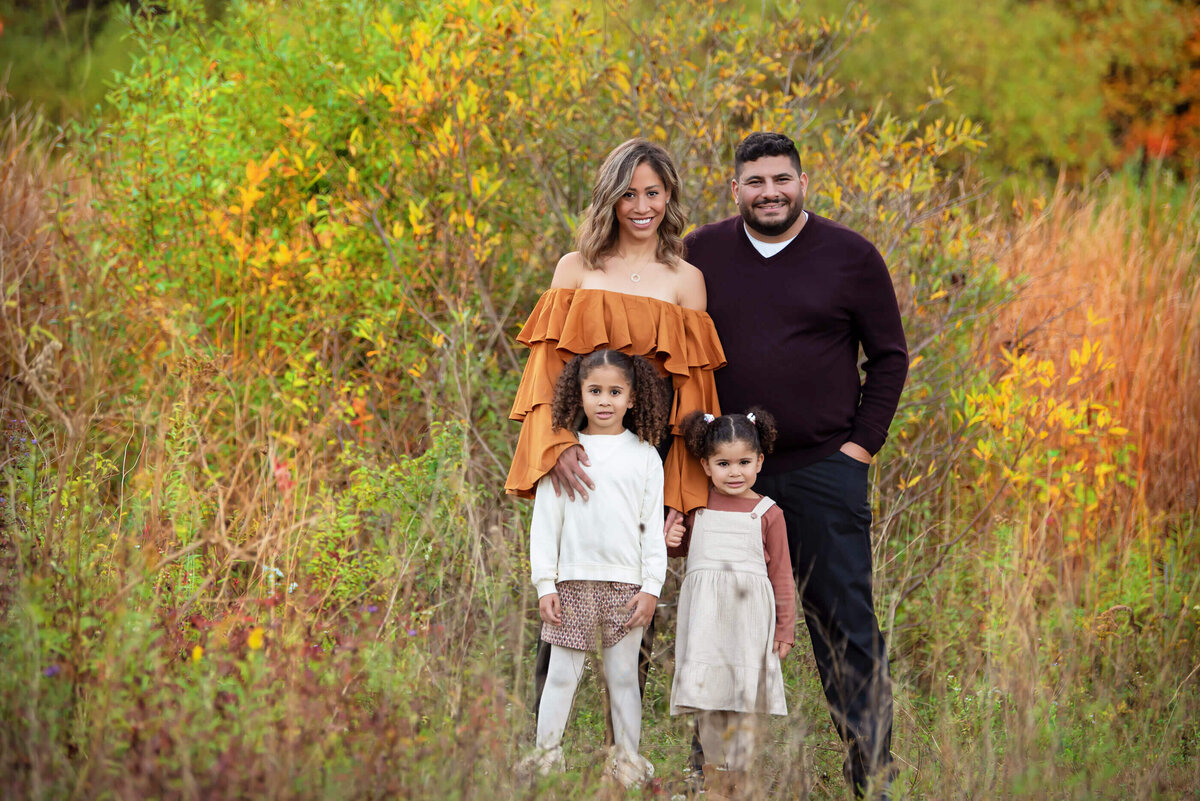 Mom and dad with their two daughters standing in tall grass for their fall family photography session in Burlington, On