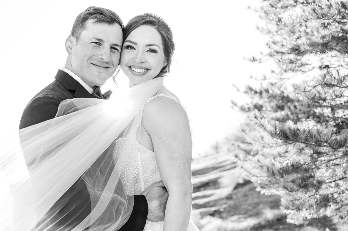 A stunning couple at sunset at The Cliffs next to a green bush as the bride's veil sweeps in front of them in a black and white photo by Raleigh wedding photographer, JoLynn Photography