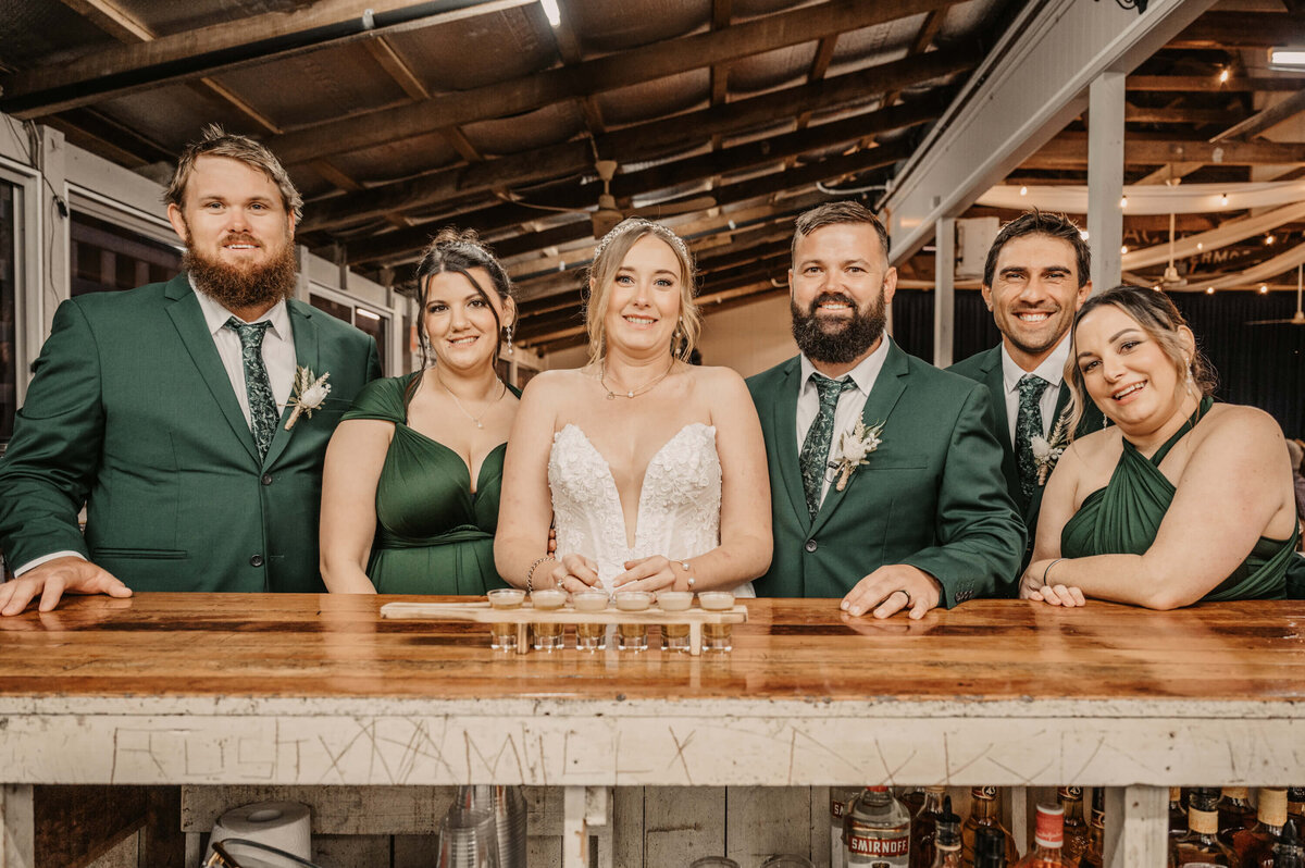 A joyful wedding party gathers at the bar, smiling and posing for a memorable group photo. - photo by Jamie Simmons