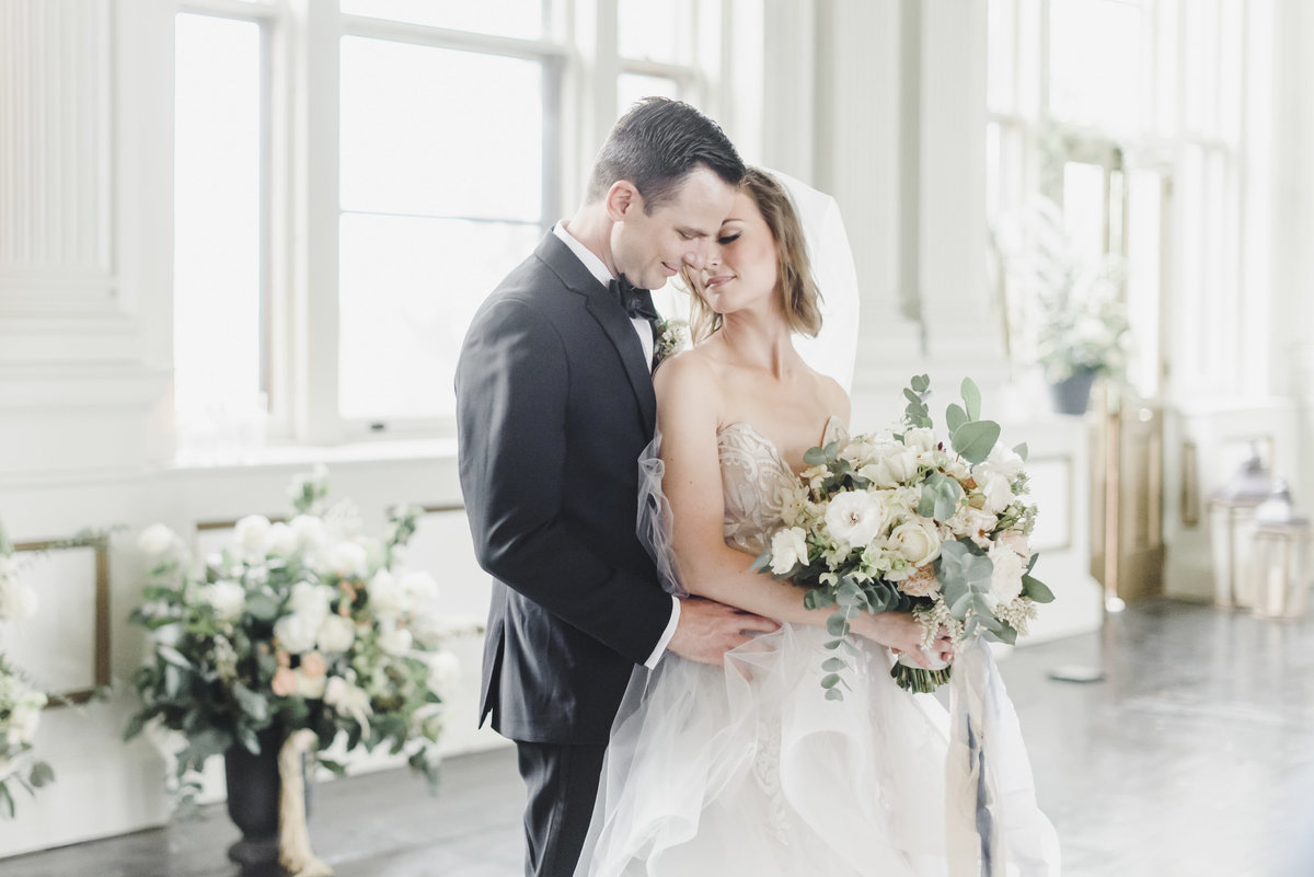 bride holds her bouquet while groom is holding her  in a romantic embrace