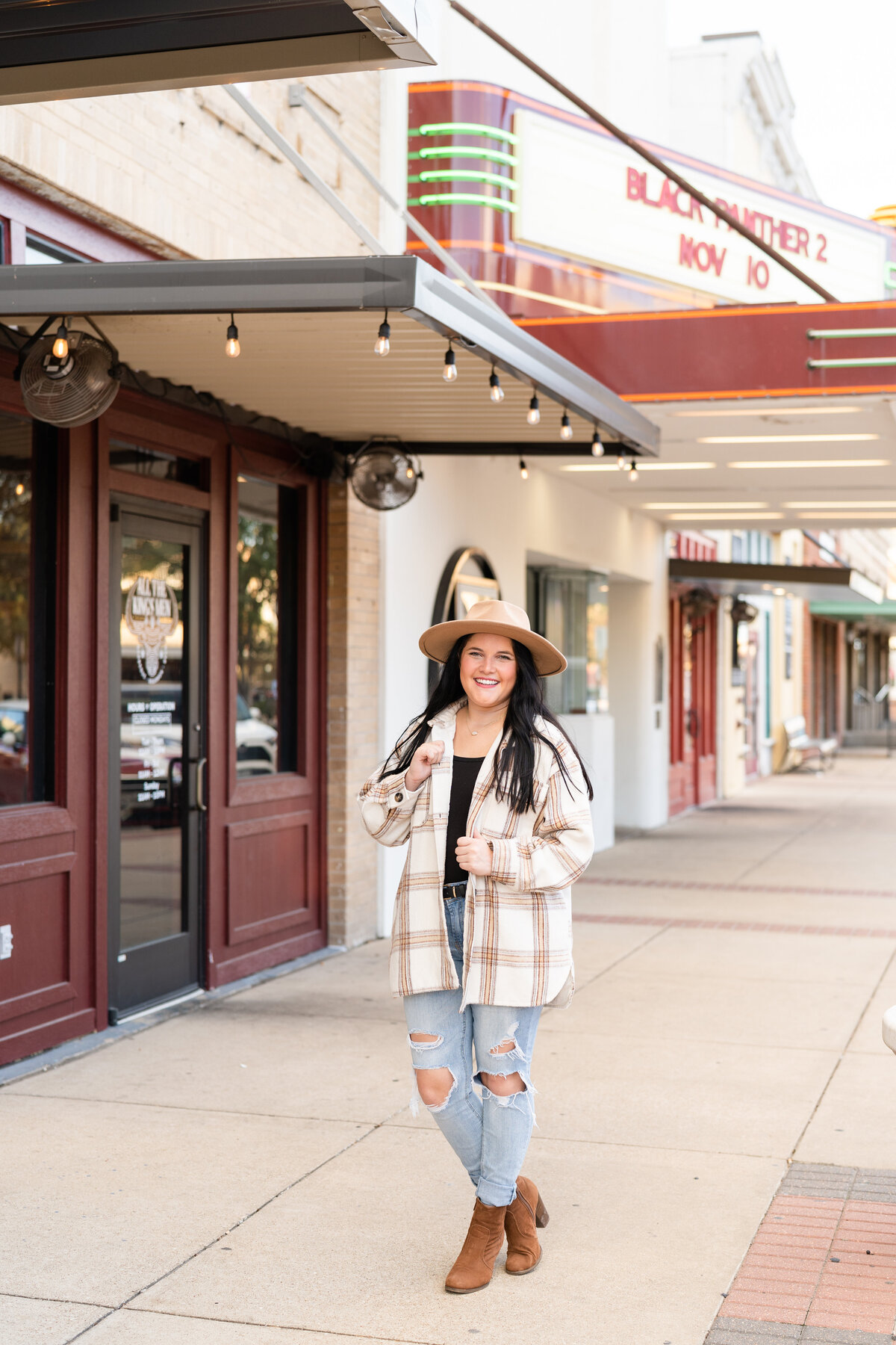 Texas A&M senior girl holding jacket and wearing flannel with cute hat and booties while standing in Downtown Bryan