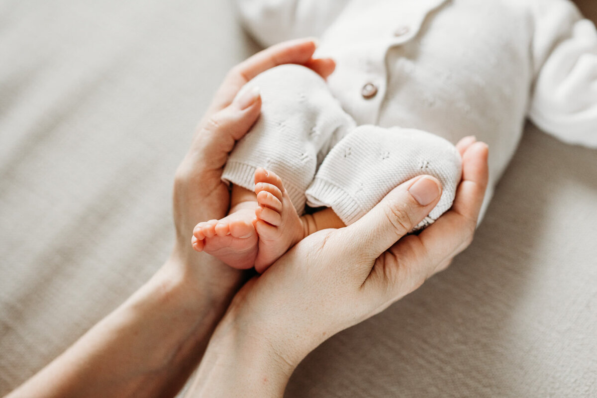 Mama houdt de voetjes van haar pasgeboren baby vast tijdens een newbornshoot.