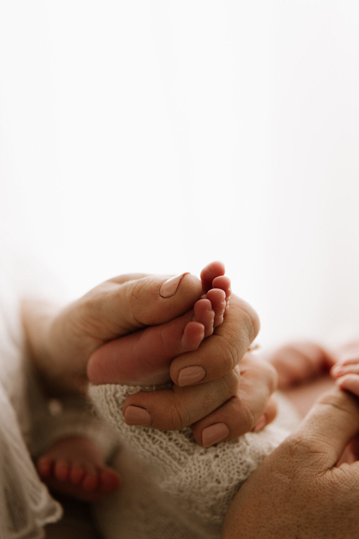 Close-up of a mother’s hands gently holding her newborn’s tiny feet, captured in a soft and airy studio setting in Southwest Sydney.