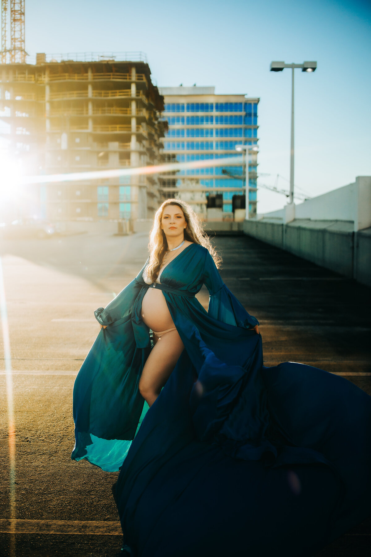 stunning backlit parking garage  pregnancy portrait with a women in a long flowy blue maternity gown