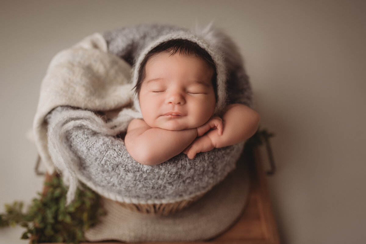 Newborn baby girl asleep at Atlanta newborn  photography studio posed in basket with chin on hands and gray fuzzy hat