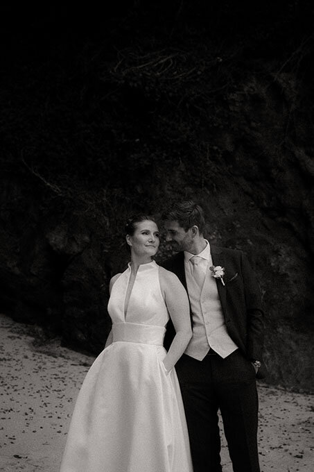 Clarisse et Corentin posant sur la plage en tenue de mariés. Photographie par Léa, photographe mariage vintage.