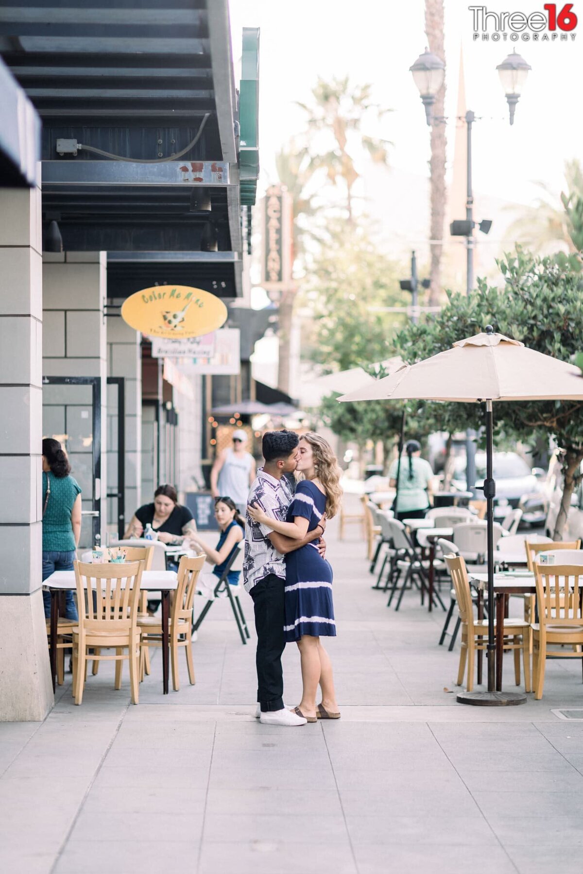 Engaged couple share a kiss on the sidewalk in Downtown Brea