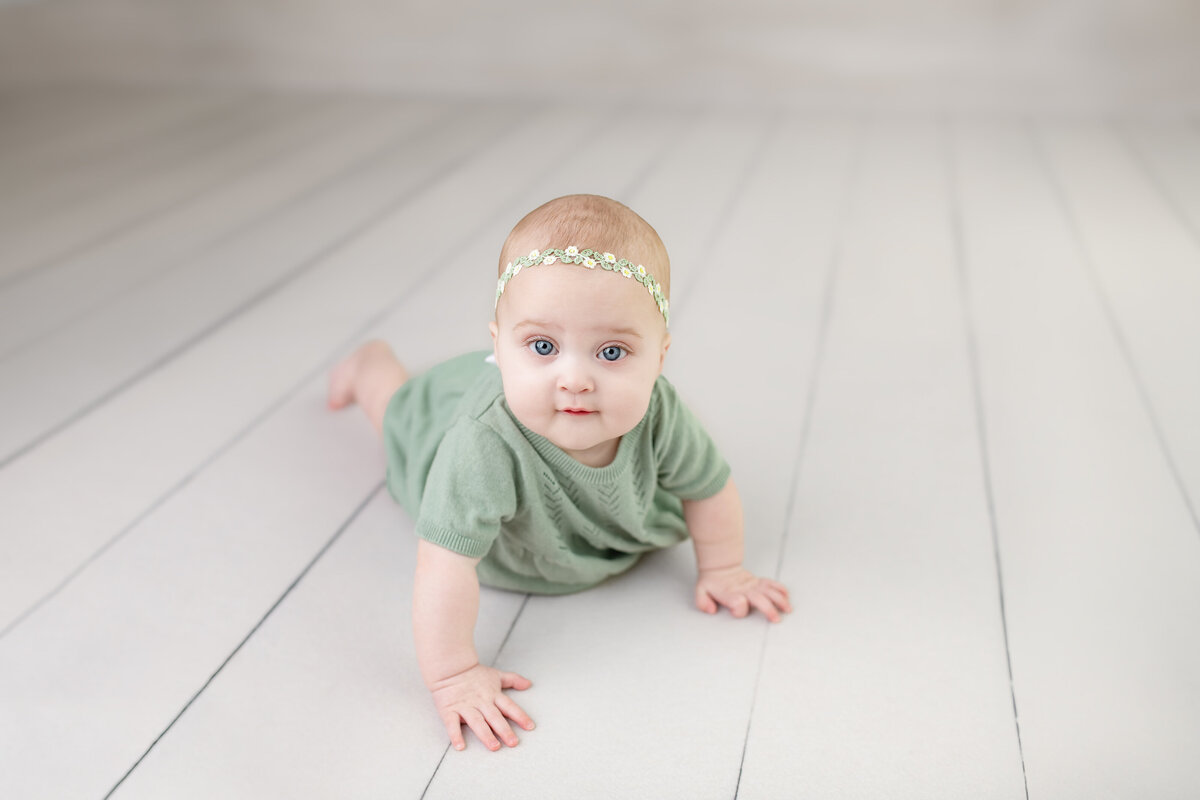 Crawling baby girl in soft green dress—captured in motion on bright white studio floors during her milestone session.