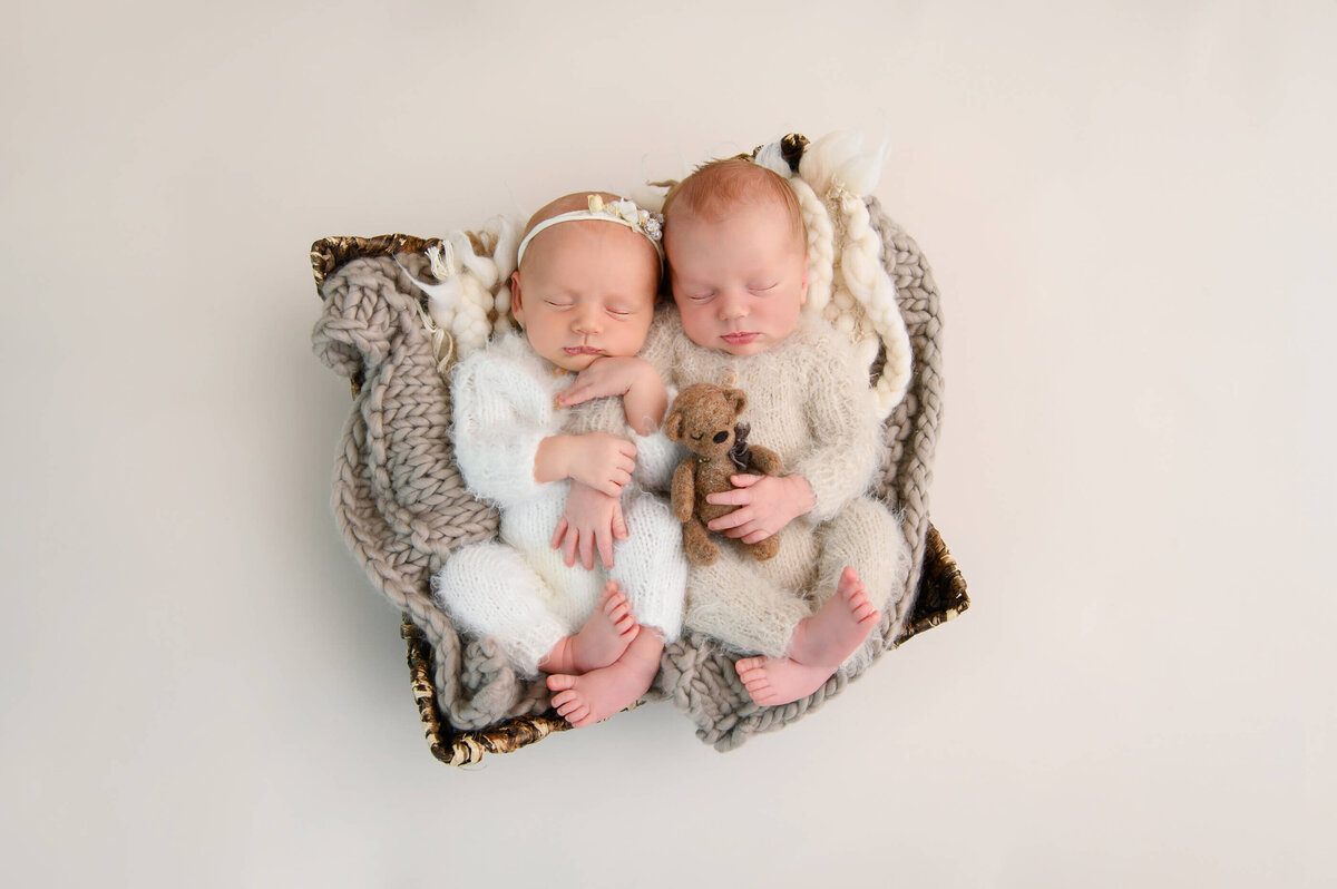 Twin newborn babies holding a tiny bear wearing fuzzy onsies for their twin newborn photography session in Burlington, Ontario.