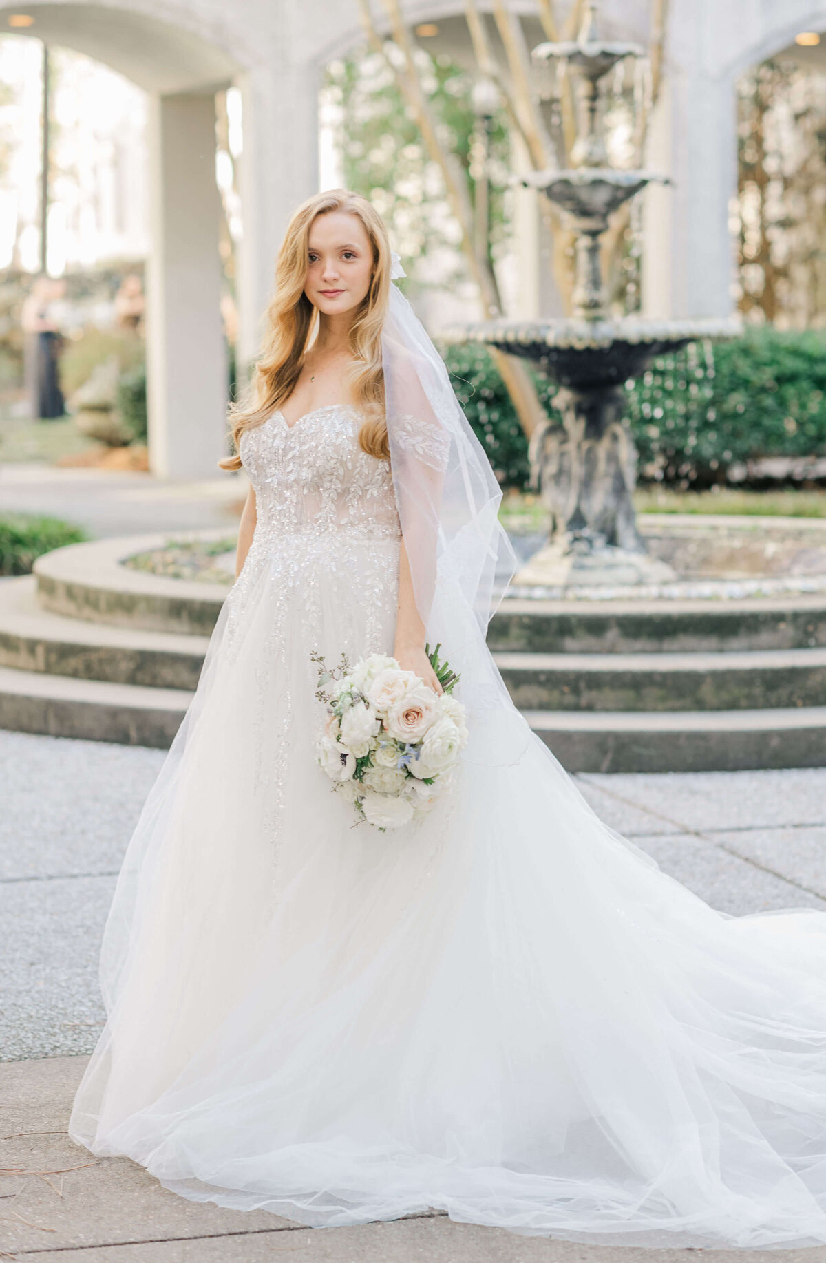 Bride standing in courtyard smiling towards camera holding bouquet
