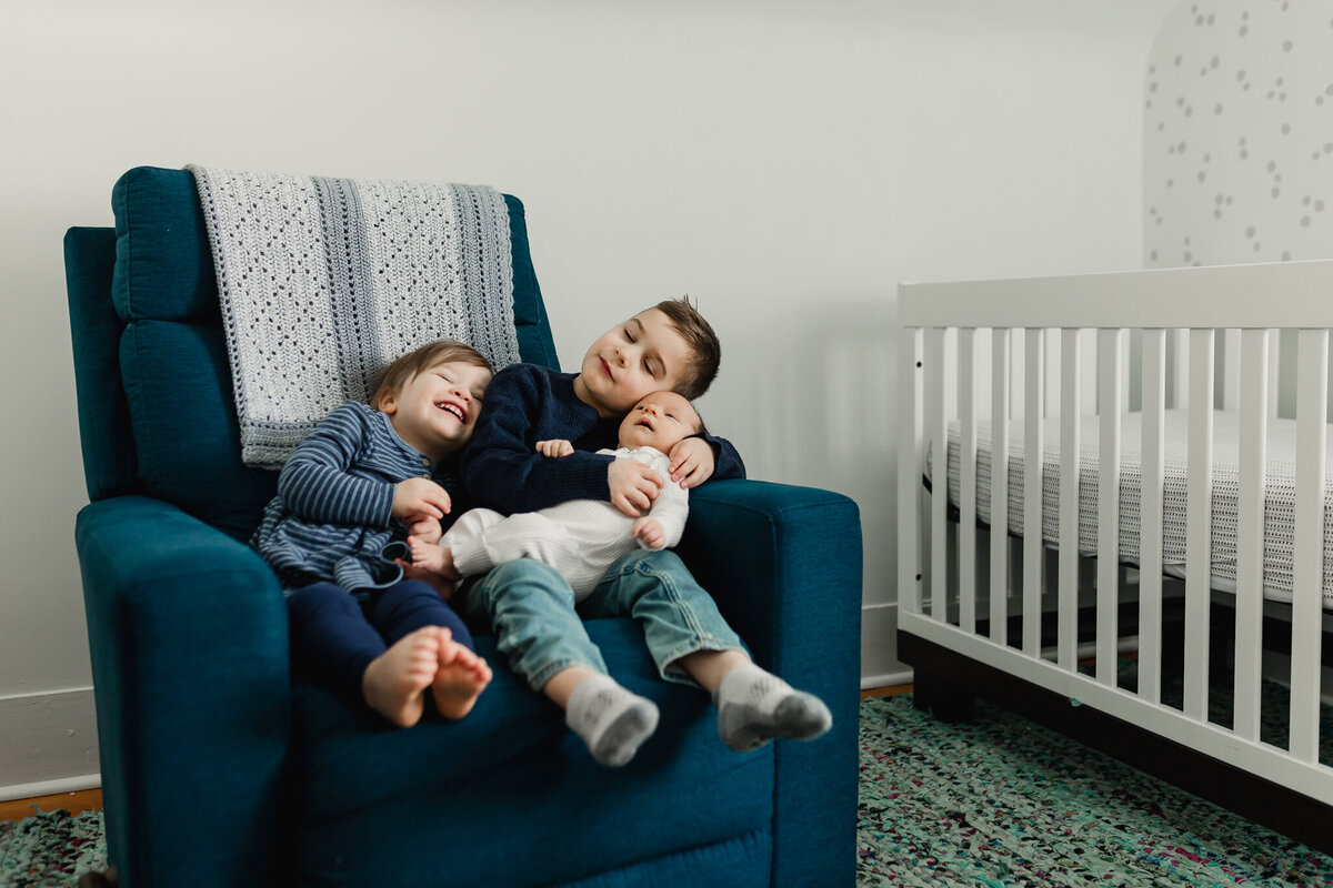 Lifestyle photography of two children sitting on a chair holding baby.