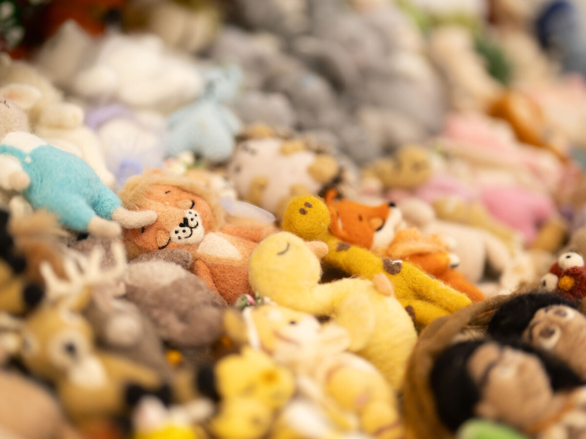 A colorful assortment of felt animal toys, including a smiling lion, reindeer, and fox, arranged closely together. The scene conveys warmth and playfulness.