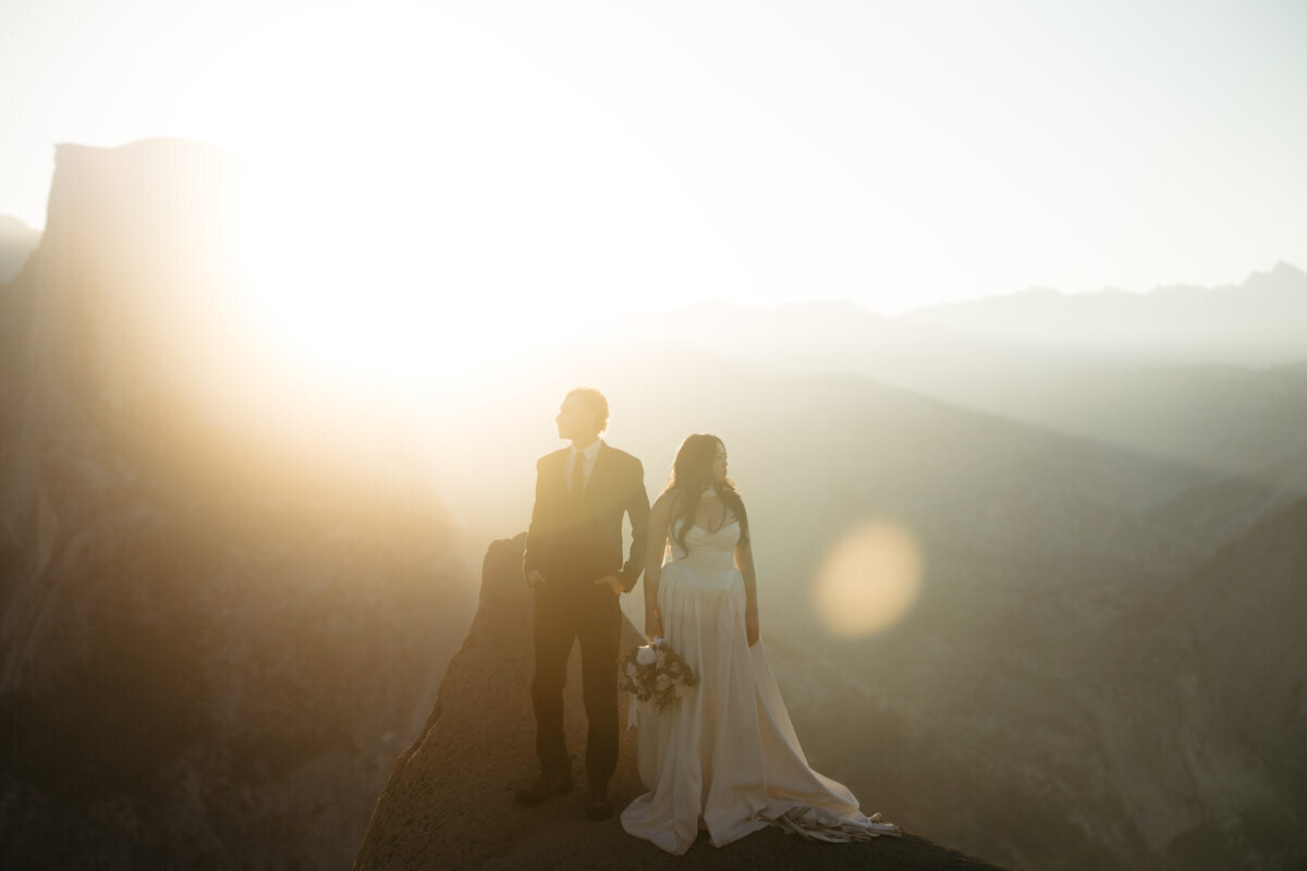 Wedding couple looks into the distance as the sunrise lights up the sky during their Glacier Point Wedding 