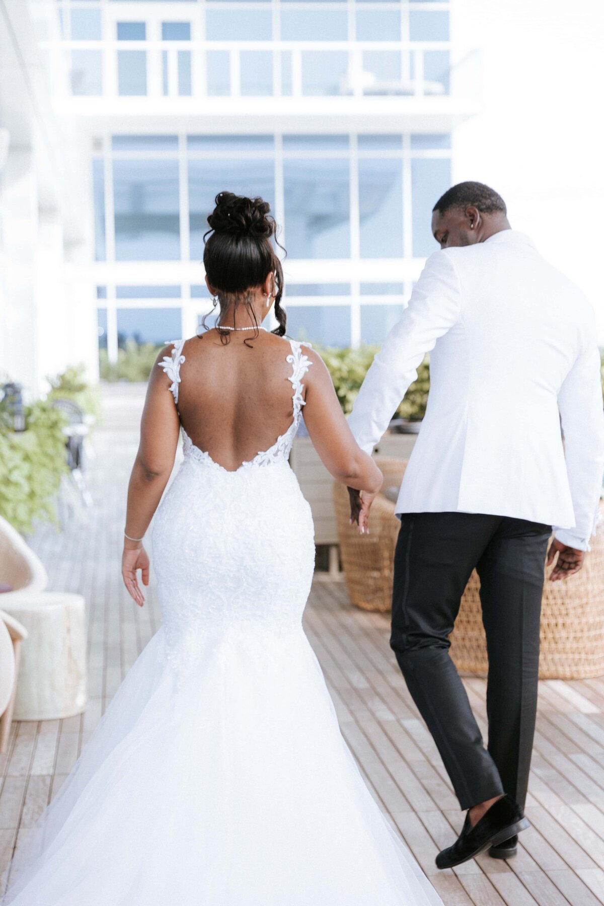 A candid moment of a newlywed couple walking hand in hand at the JW Marriott Bonnet Creek in Orlando, Florida. The bride wears a fitted lace gown with an open back and floral straps, while the groom is dressed in a sharp white tuxedo jacket. Captured from behind, the image highlights their effortless style and connection. This modern, true-to-color wedding photo was taken by Phavy Photography—a St. Augustine wedding photographer known for timeless, documentary-style storytelling across Florida.
