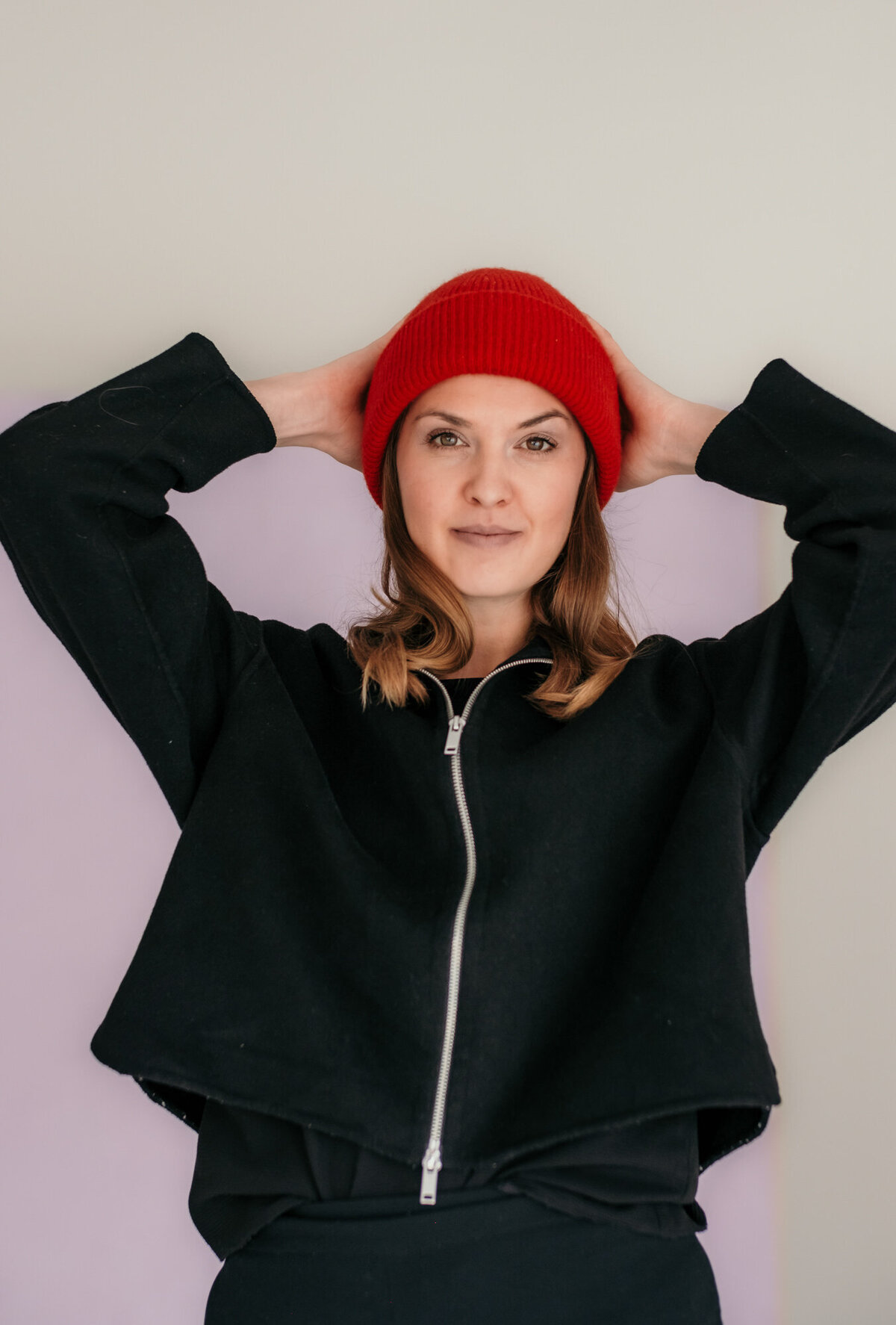 Portrait of woman with red beanie holds her hat with both hands.