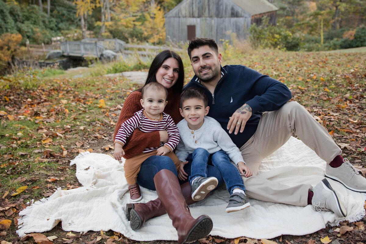 Family of four snuggled on a blanket in the fall smiling